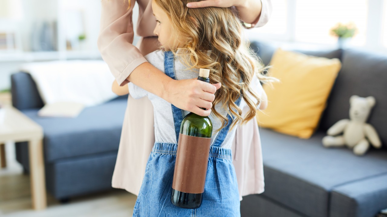 Mutter umarmt Mädchen mit einer Flasche Wein in der Hand