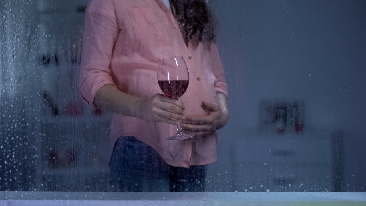 Schwangere Frau hält mit der einen Hand ihren Bauch und mit der anderen ein Glas Rotwein